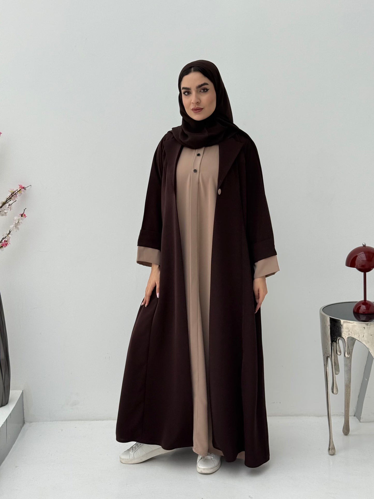 Woman wearing a dark brown and beige abaya with amathcing sheila on a white background