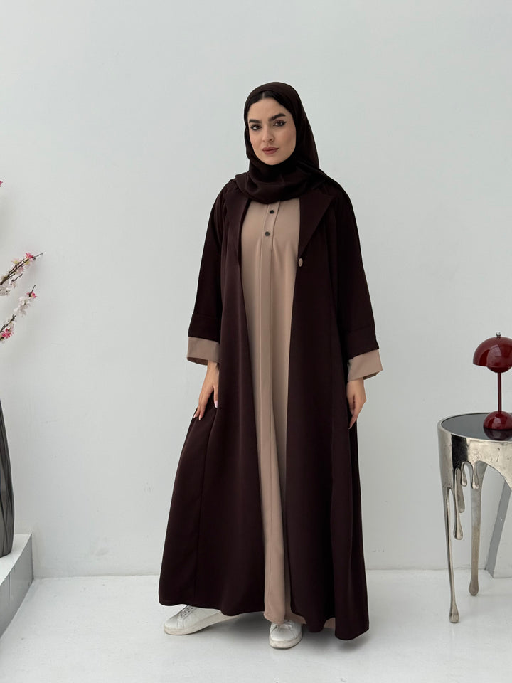Woman wearing a dark brown and beige abaya with amathcing sheila on a white background