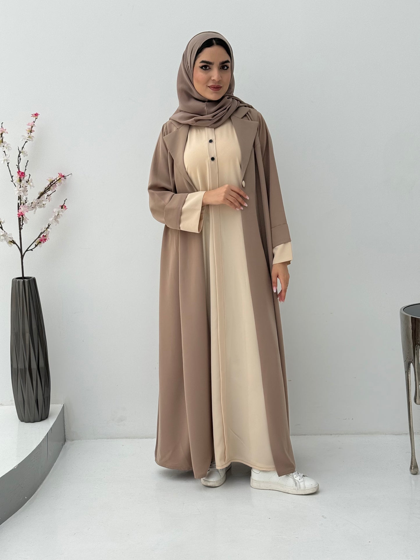 Woman wearing a Light Brown Cream Abaya with a matching sheila, standing in a minimalistic room.