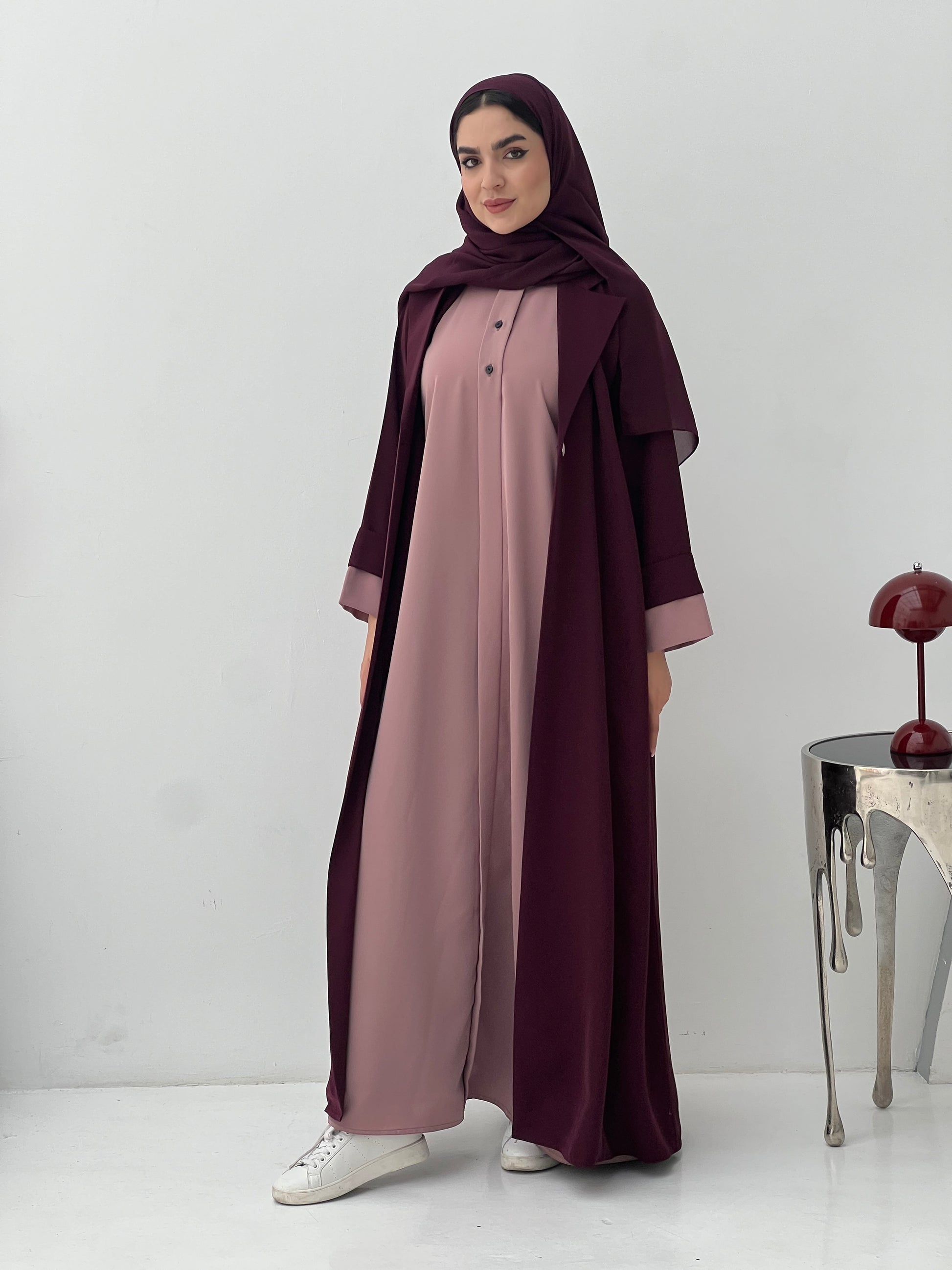 Woman wearing a long, Maroon and Dusty Pink Abaya with a matching sheila hijab on a white background