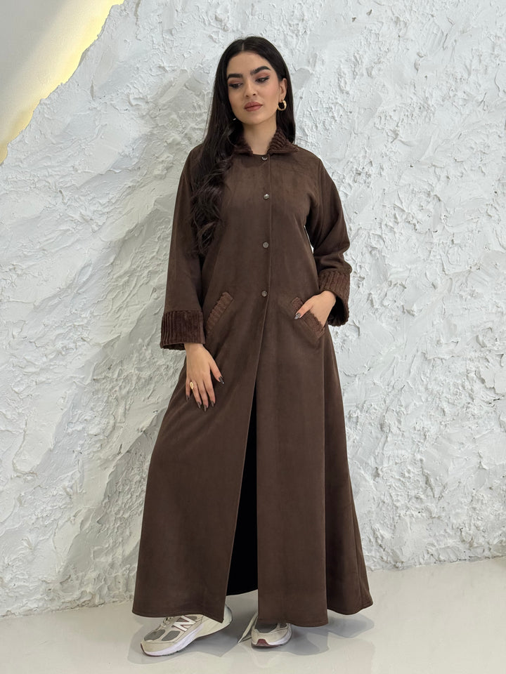 A woman wearing a long Dark Brown Shamwa Abaya Set standing on a textured white floor.