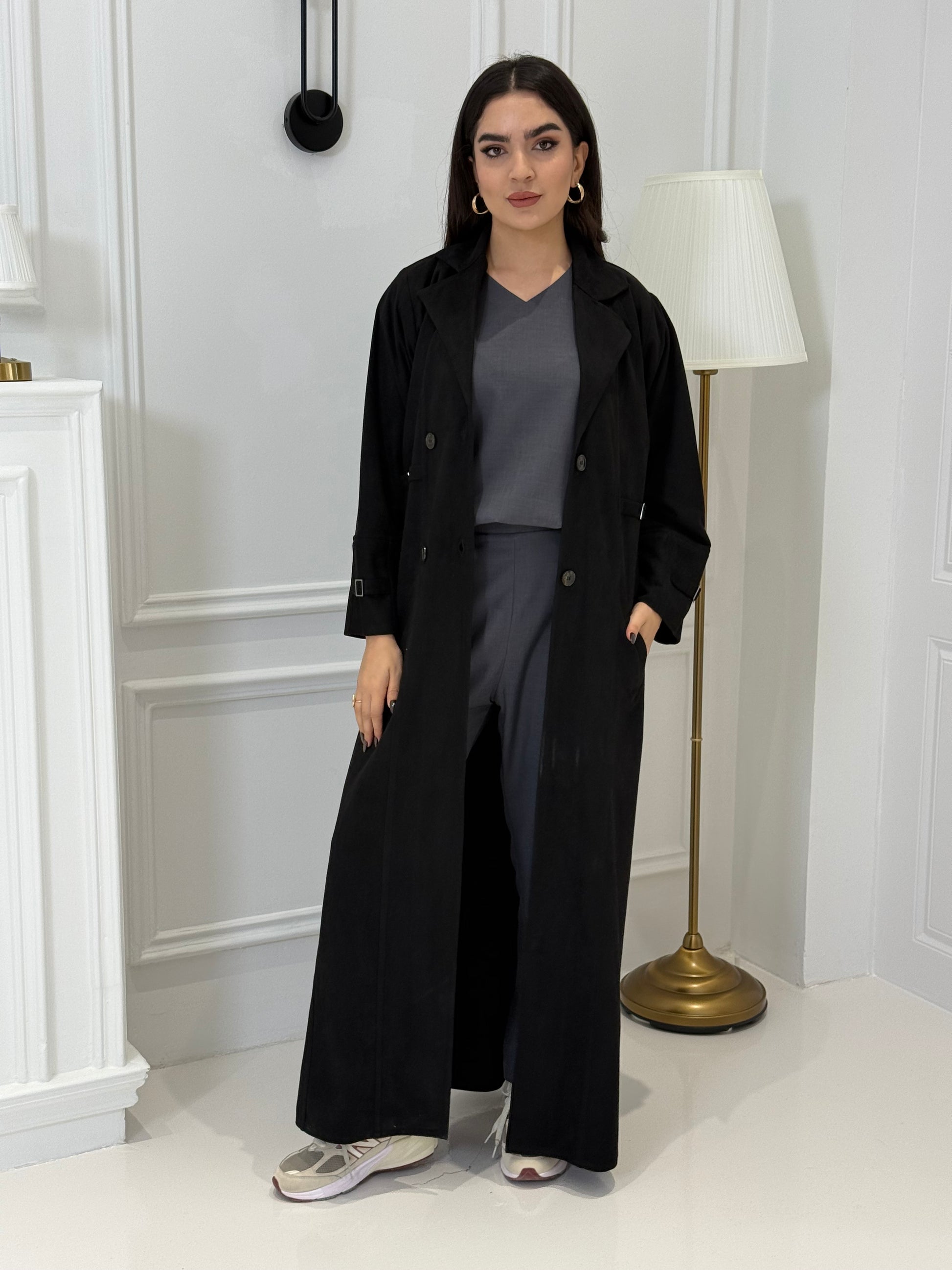 Woman wearing a Black Shamwa Trench Abaya Set standing in a room with white walls and a door.