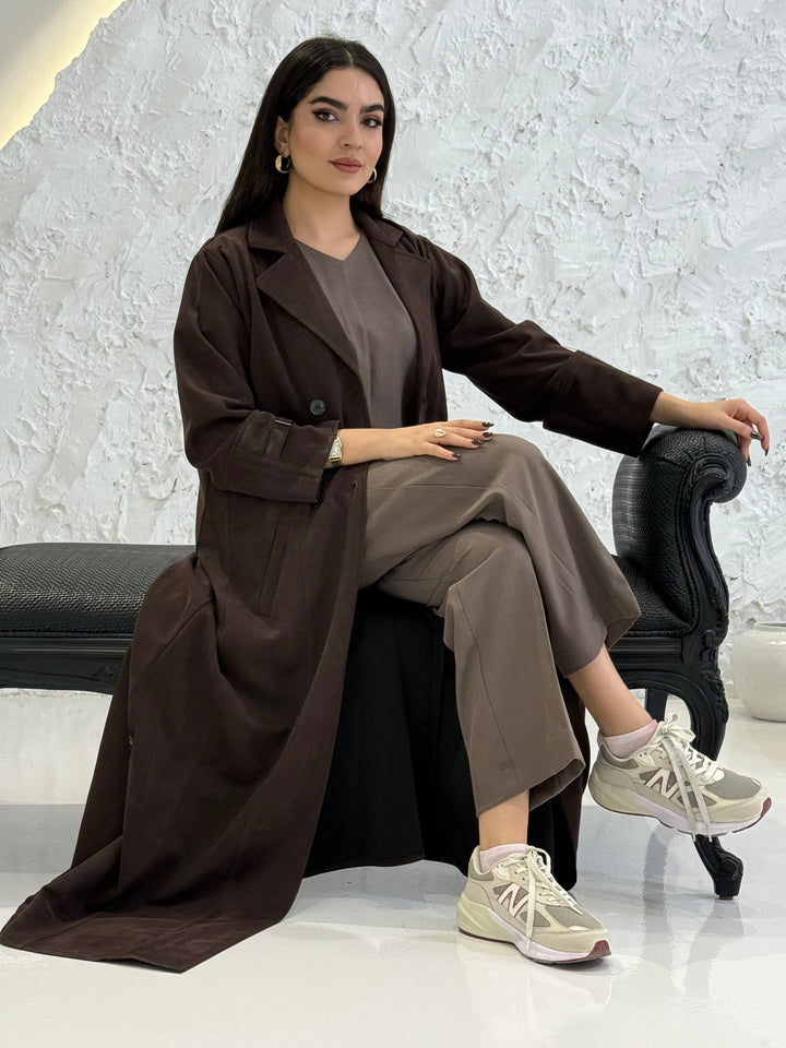 Woman in a Dark Brown Shamwa Trench Abaya Set posing against a white textured wall.
