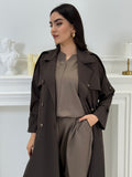 Person wearing a long Dark Brown Linen coat Abaya Set standing in front of a white door with gold handles.