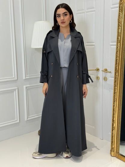 Person wearing a long Dark Grey Linen Abaya trench coat Set standing in front of a white door with gold handles.