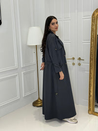 Person wearing a long Dark Grey Linen Abaya trench coat Set standing in front of a white door with gold handles.