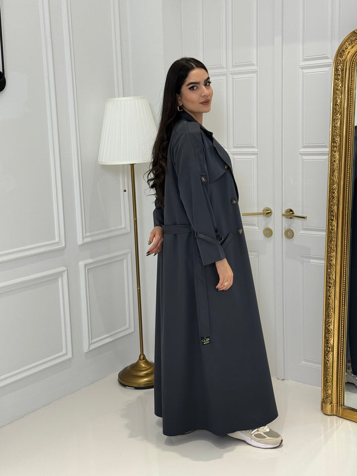 Person wearing a long Dark Grey Linen Abaya trench coat Set standing in front of a white door with gold handles.