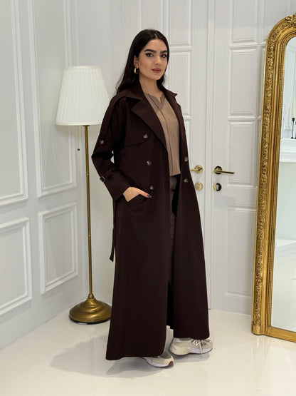 Person wearing a long Dark maroon Linen Abaya trench coat Set standing in front of a white door with gold handles.