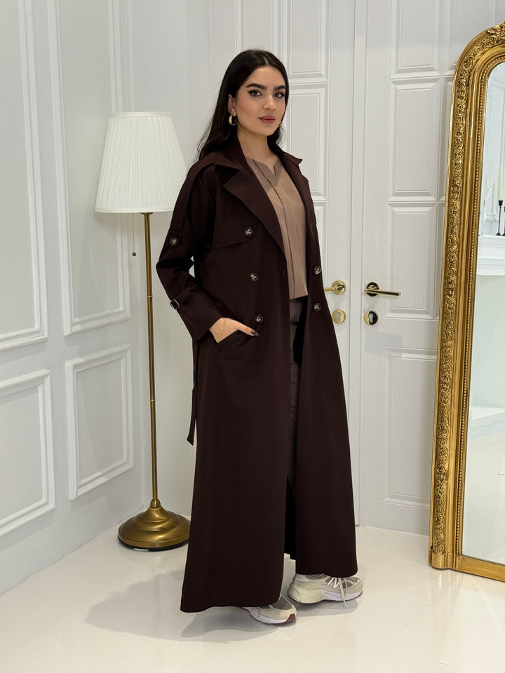 Person wearing a long Dark maroon Linen Abaya trench coat Set standing in front of a white door with gold handles.