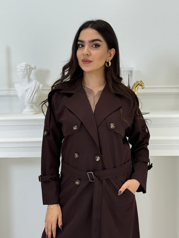 Person wearing a long Dark maroon Linen Abaya trench coat Set standing in front of a white door with gold handles.