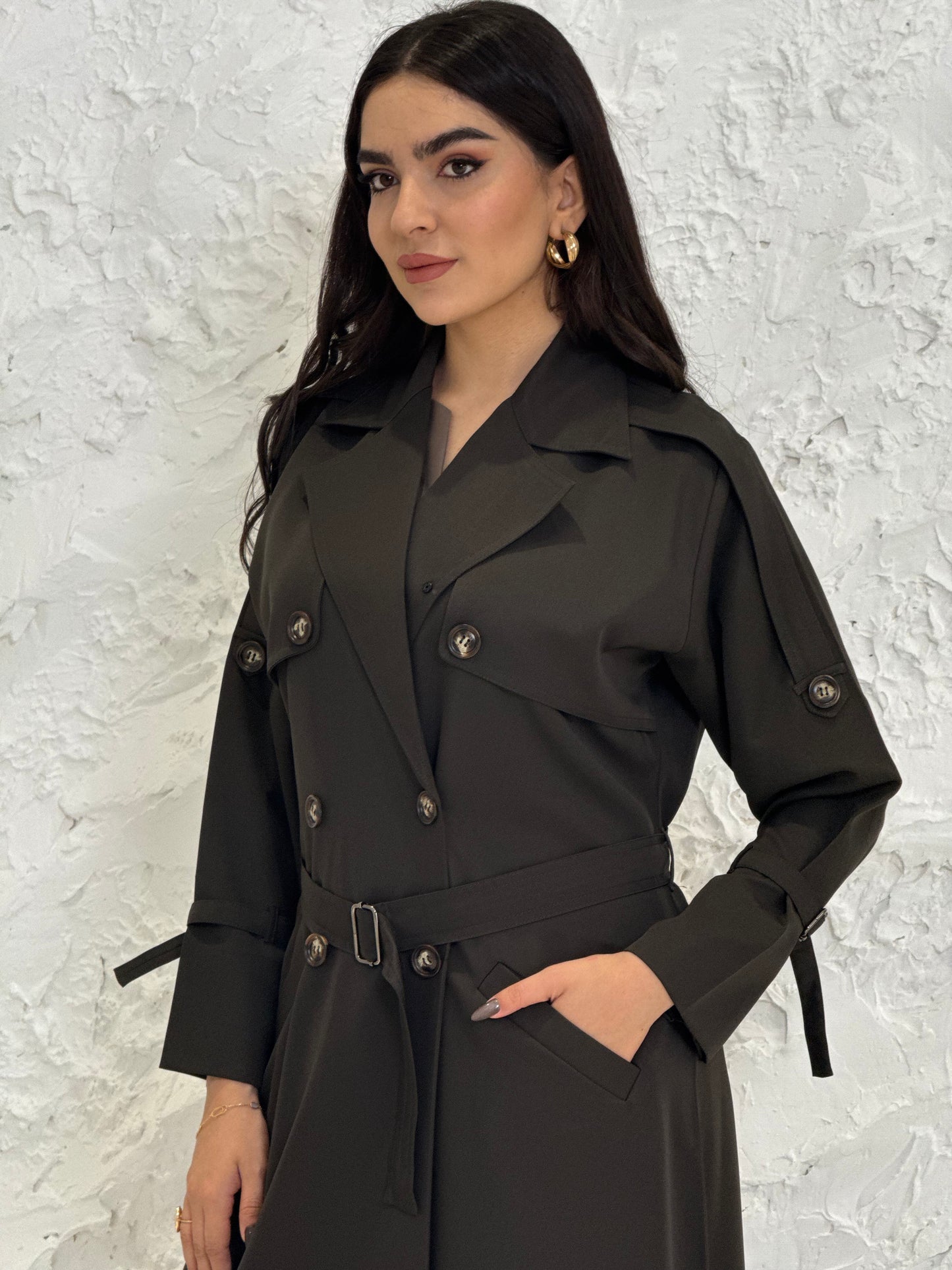 Person wearing a long Dark olive Linen Abaya trench coat Set standing in front of a white door with gold handles.