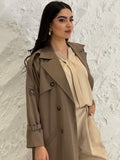 Person wearing a long light brownLinen Abaya trench coat Set standing in front of a white door with gold handles.
