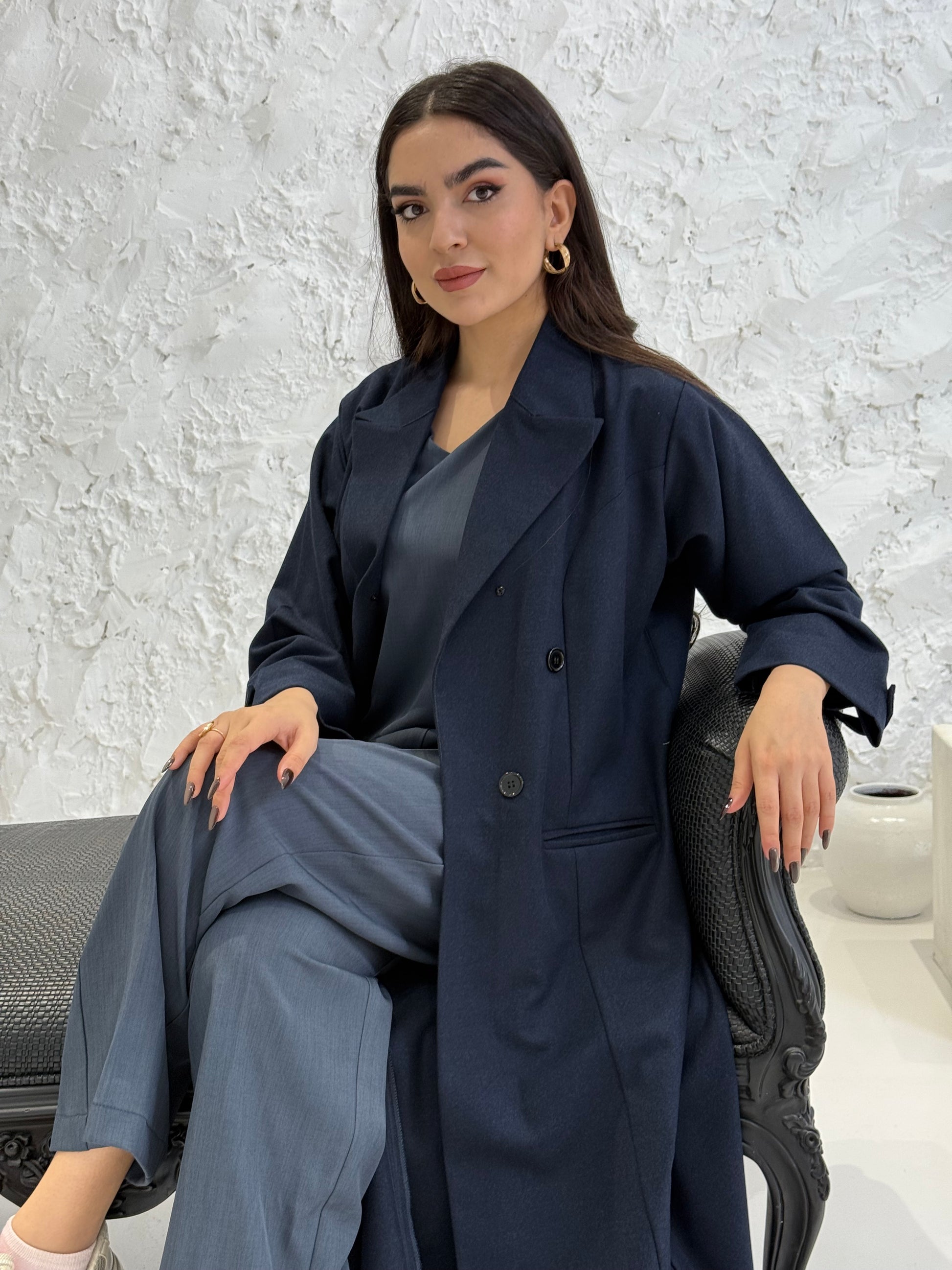 Woman wearing a long navy blue Jookh Abaya Set standing in front of a white wall with a gold-framed mirror.