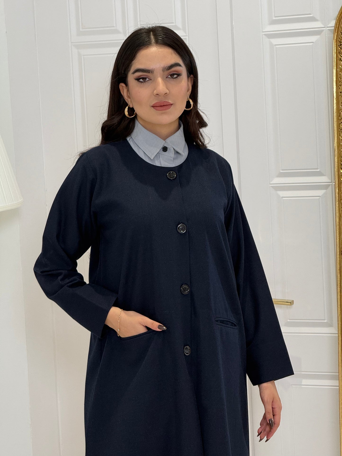 Woman wearing a navy blue coat jookh abaya and gray pants, holding a black handbag.