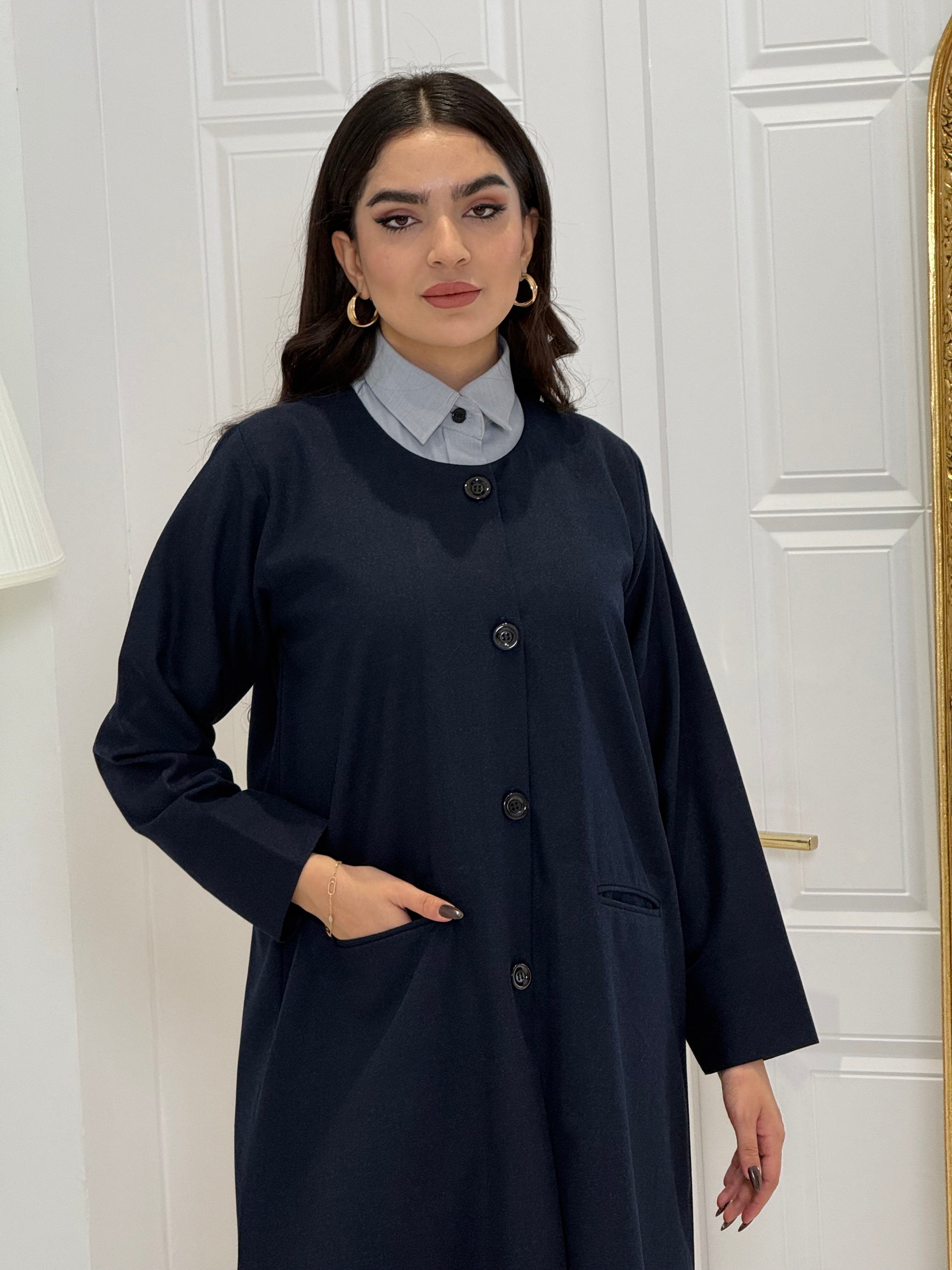 Woman wearing a navy blue coat jookh abaya and gray pants, holding a black handbag.