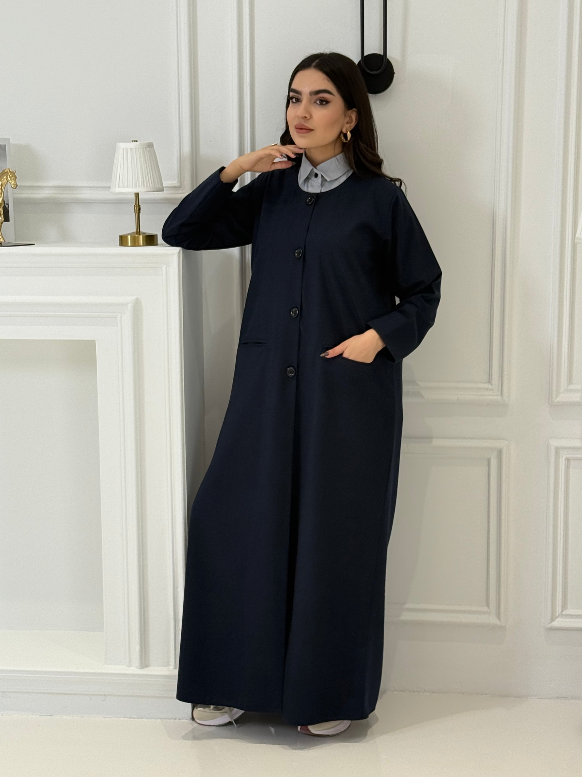 Woman wearing a navy blue coat jookh abaya and gray pants, holding a black handbag.
