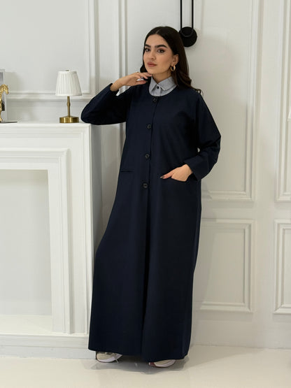 Woman wearing a navy blue coat jookh abaya and gray pants, holding a black handbag.