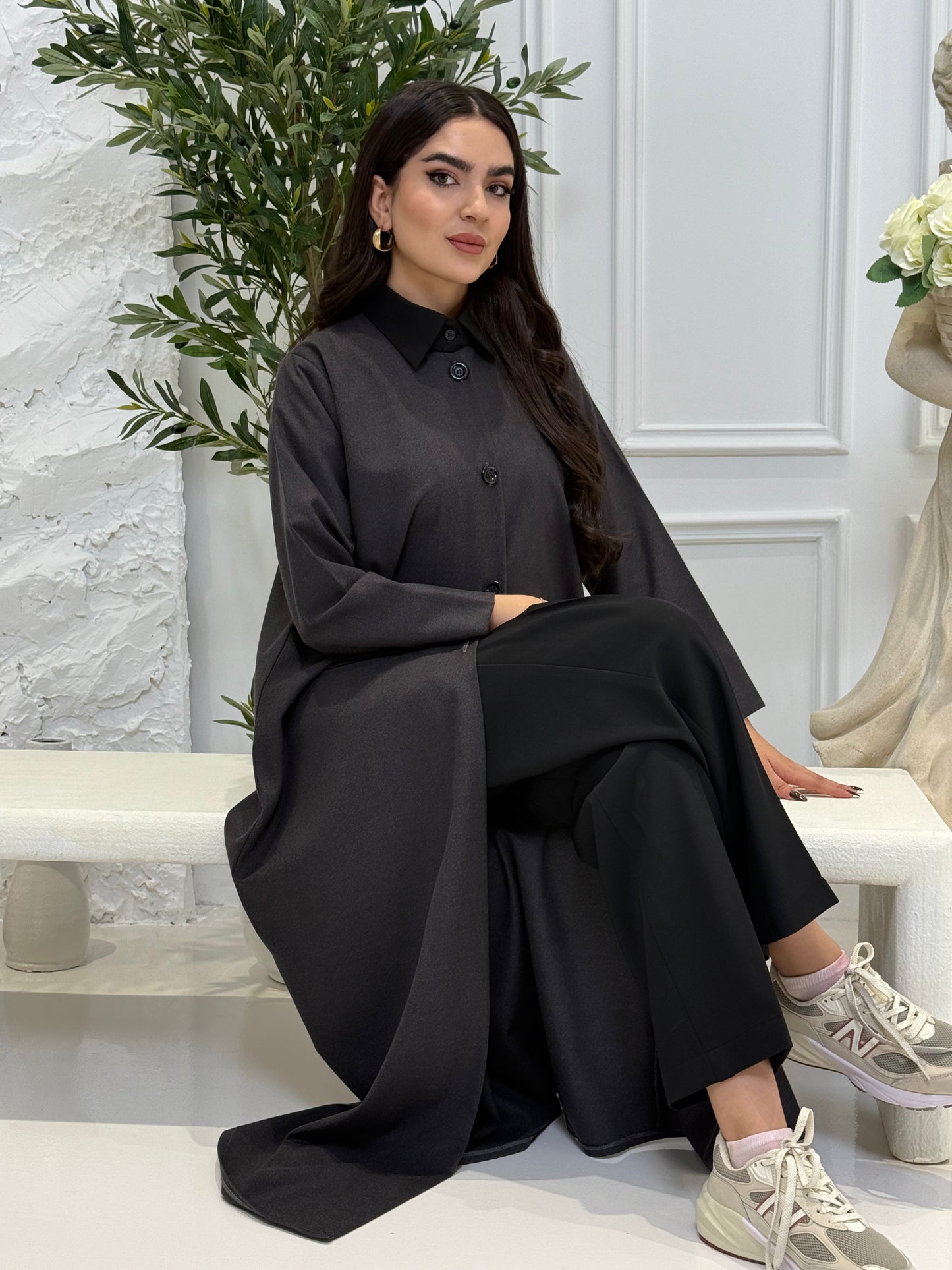 Woman wearing a dark grey coat jookh abaya and gray pants, holding a black handbag.