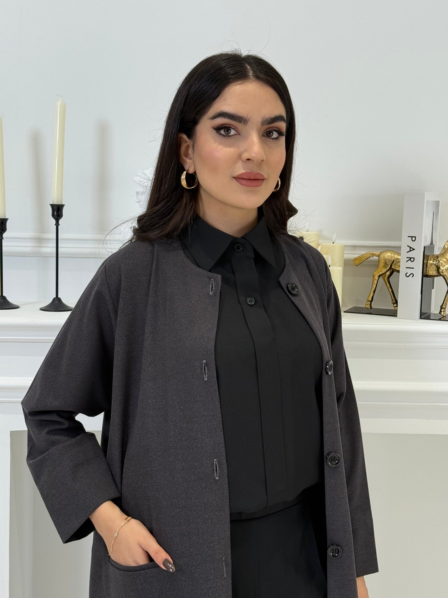 Woman wearing a dark grey coat jookh abaya and gray pants, holding a black handbag.