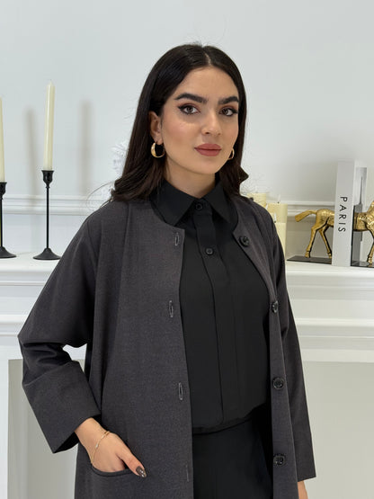 Woman wearing a dark grey coat jookh abaya and gray pants, holding a black handbag.