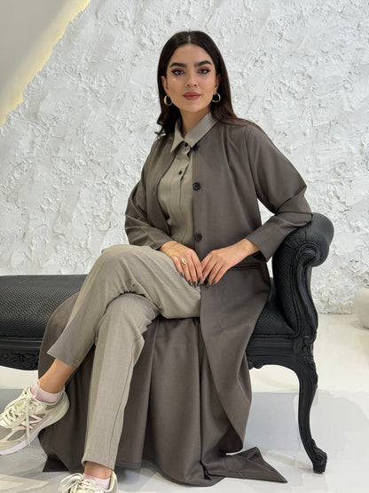 Woman wearing a dark taupe coat jookh abaya and gray pants, holding a black handbag.