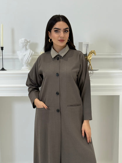 Woman wearing a dark taupe coat jookh abaya and gray pants, holding a black handbag.