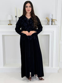 A woman wearing a long navy blue Velvet Embroidered Abaya standing against a white decoration 