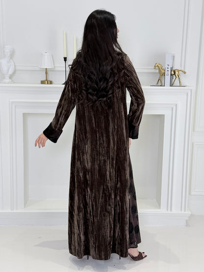 woman wearing a dark brown plissé velvet abaya coat standing in front of a white door with gold handles.