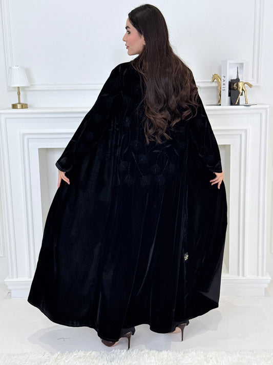 Woman wearing a premium luxury black Floral Velvet Abaya dress with floral embellishments in a white room.