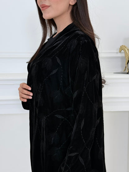 Woman wearing a premium luxury black Floral Velvet Abaya dress with floral embellishments in a white room.