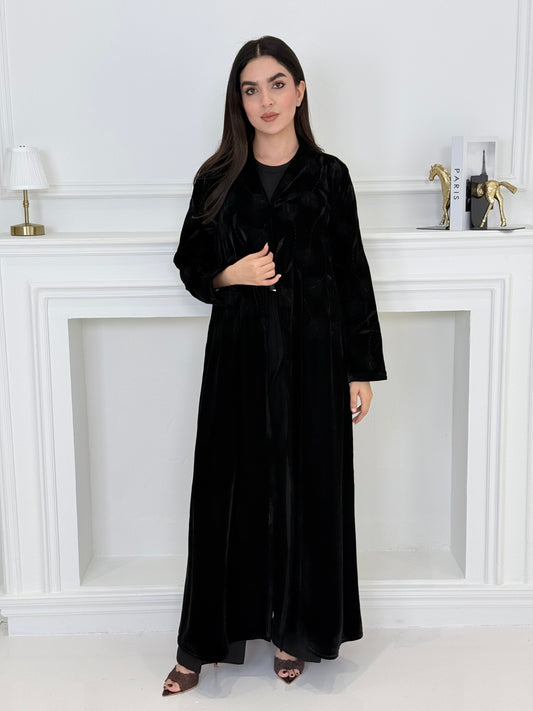 Woman wearing a premium luxury black Floral Velvet Abaya dress with floral embellishments in a white room.