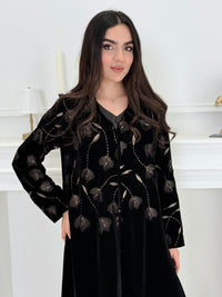 Woman wearing a premium luxury black and Gold Floral Velvet Abaya dress with floral embellishments in a white room.