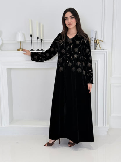 Woman wearing a premium luxury black and Gold Floral Velvet Abaya dress with floral embellishments in a white room.