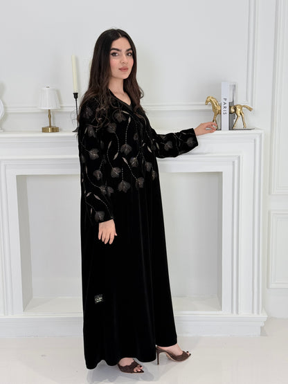 Woman wearing a premium luxury black and Gold Floral Velvet Abaya dress with floral embellishments in a white room.