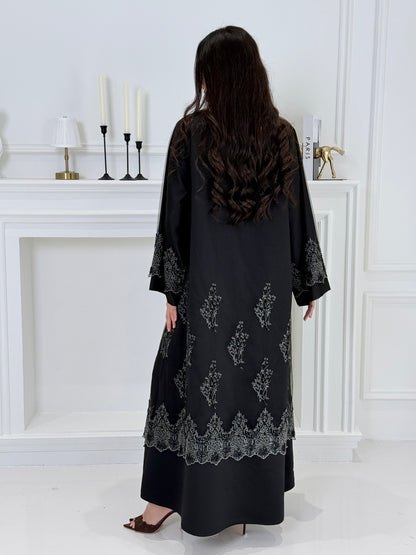 Woman wearing a Premium Silver Embroidered Black Abaya dress with lace details made from Nida fabric and matchhing sheila in a white room.