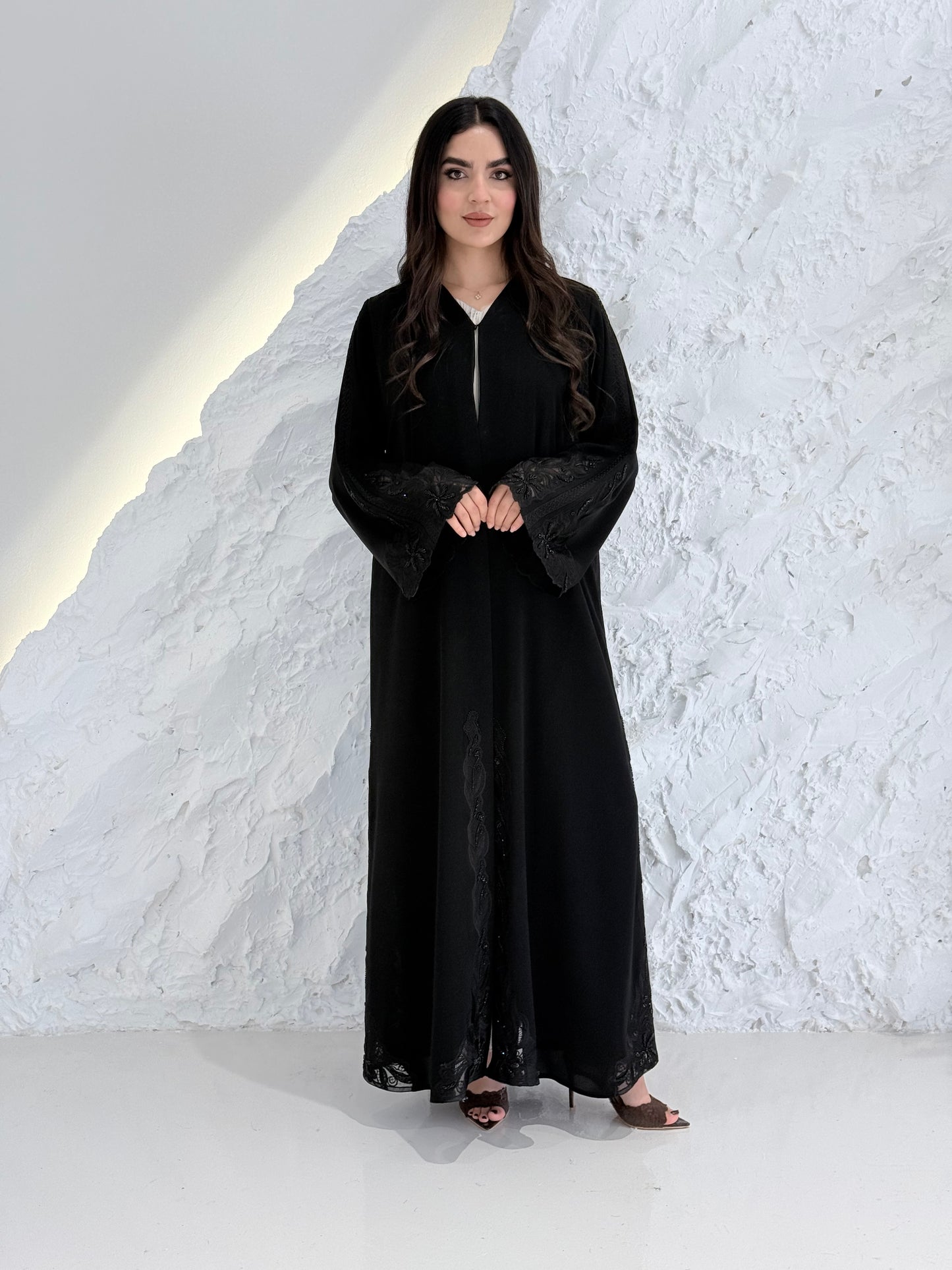 Person wearing a Premium Luxury Hand-Embellished Black Abaya outfit made from Nida fabric, standing on a textured white surface