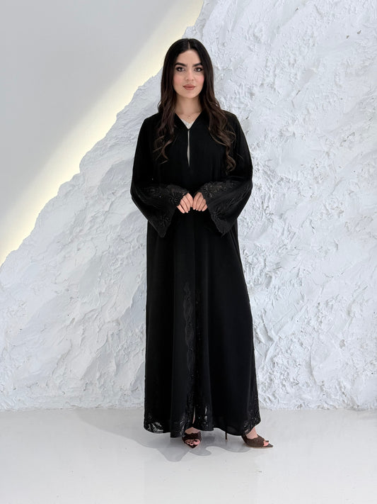 Person wearing a Premium Luxury Hand-Embellished Black Abaya outfit made from Nida fabric, standing on a textured white surface
