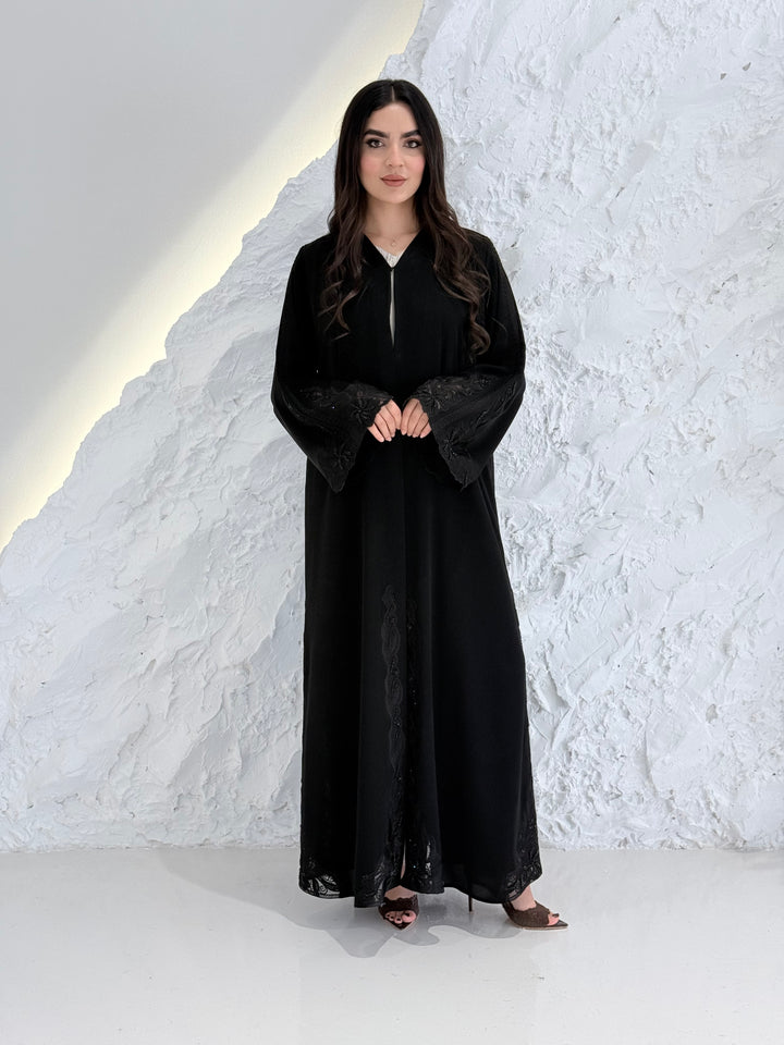 Person wearing a Premium Luxury Hand-Embellished Black Abaya outfit made from Nida fabric, standing on a textured white surface