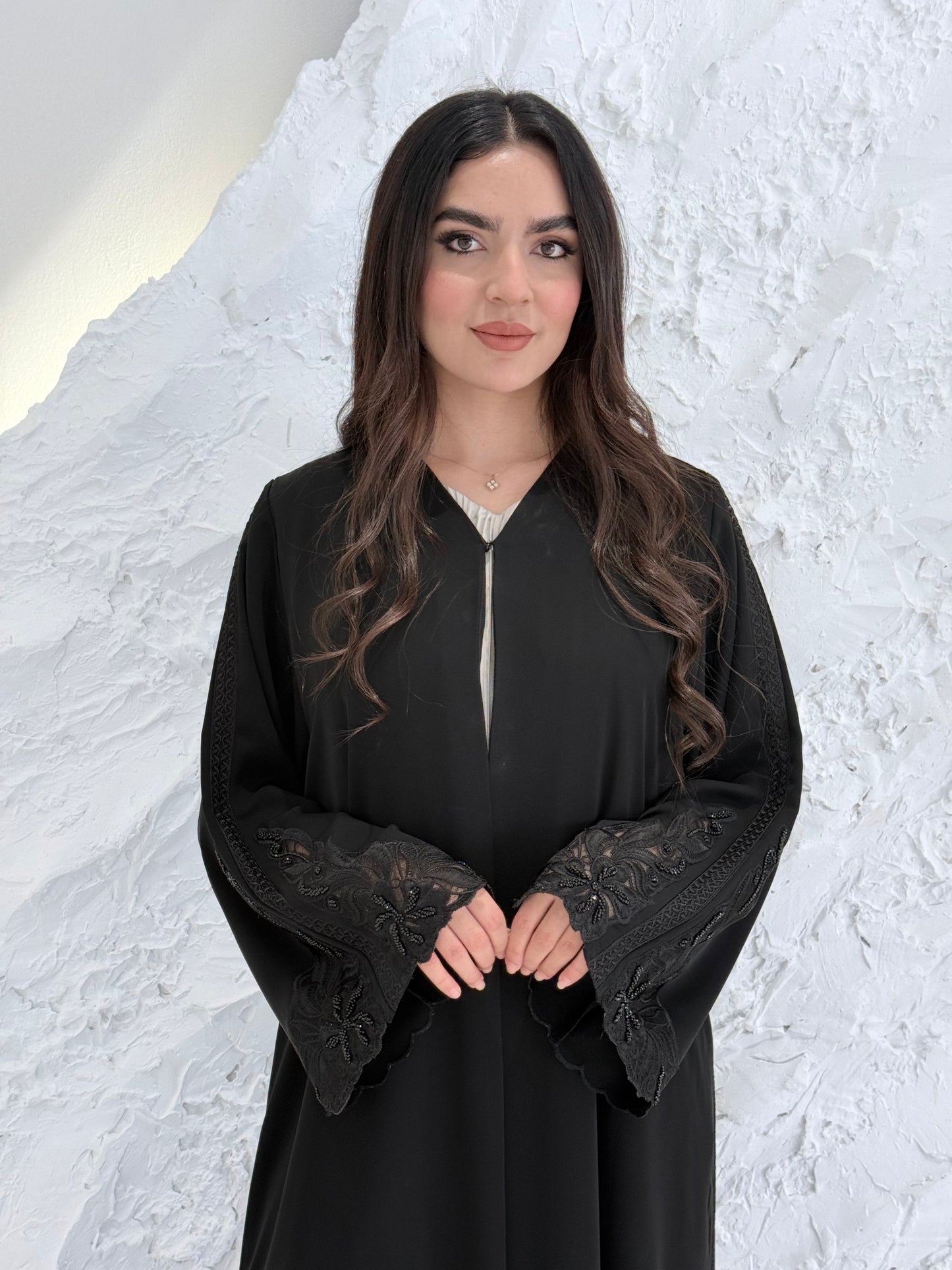 Person wearing a Premium Luxury Hand-Embellished Black Abaya outfit made from Nida fabric, standing on a textured white surface