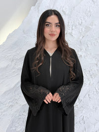 Person wearing a Premium Luxury Hand-Embellished Black Abaya outfit made from Nida fabric, standing on a textured white surface