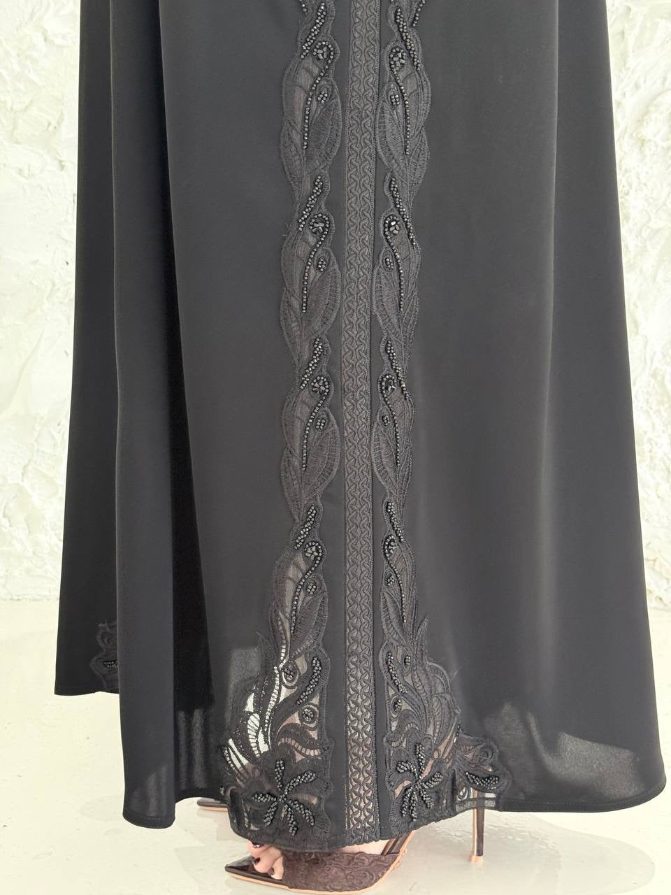 Person wearing a Premium Luxury Hand-Embellished Black Abaya outfit made from Nida fabric, standing on a textured white surface