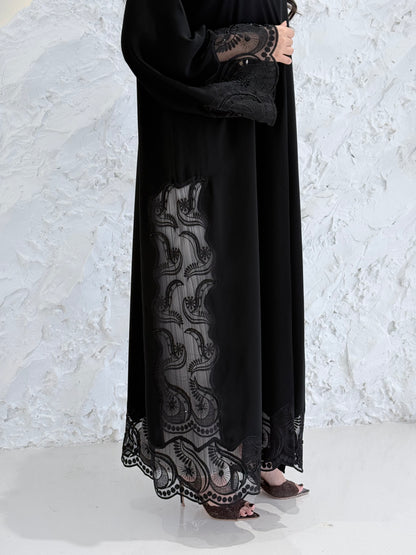 Woman wearing a Premium Black Hand-Embellished Abaya with lace details against a white textured wall.