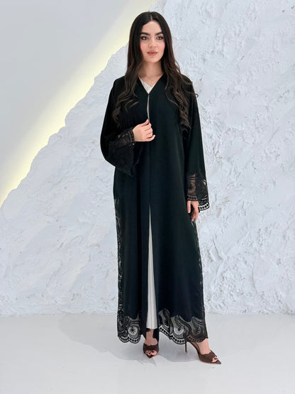 Woman wearing a Premium Black Hand-Embellished Abaya with lace details against a white textured wall.
