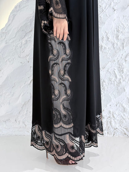 Woman wearing a Premium Gold Hand-Embellished Abaya with lace details against a white textured wall.