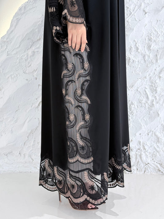 Woman wearing a Premium Gold Hand-Embellished Abaya with lace details against a white textured wall.