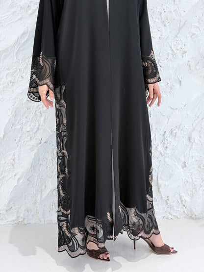 Woman wearing a Premium Gold Hand-Embellished Abaya with lace details against a white textured wall.
