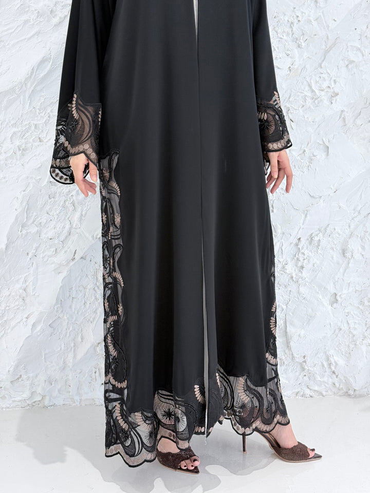 Woman wearing a Premium Gold Hand-Embellished Abaya with lace details against a white textured wall.