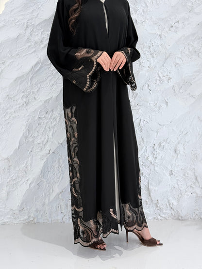 Woman wearing a Premium Gold Hand-Embellished Abaya with lace details against a white textured wall.