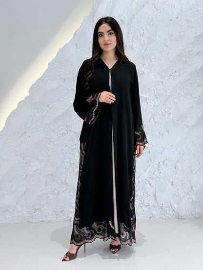 Woman wearing a Premium Gold Hand-Embellished Abaya with lace details against a white textured wall.