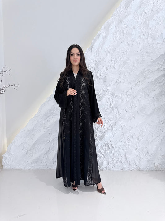 Woman wearing a Premium Black Hand-Embellished Abaya against a white textured wall